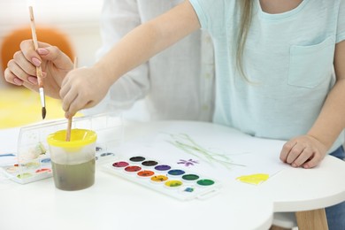 Photo of Mother and her little daughter painting with watercolor at home, closeup