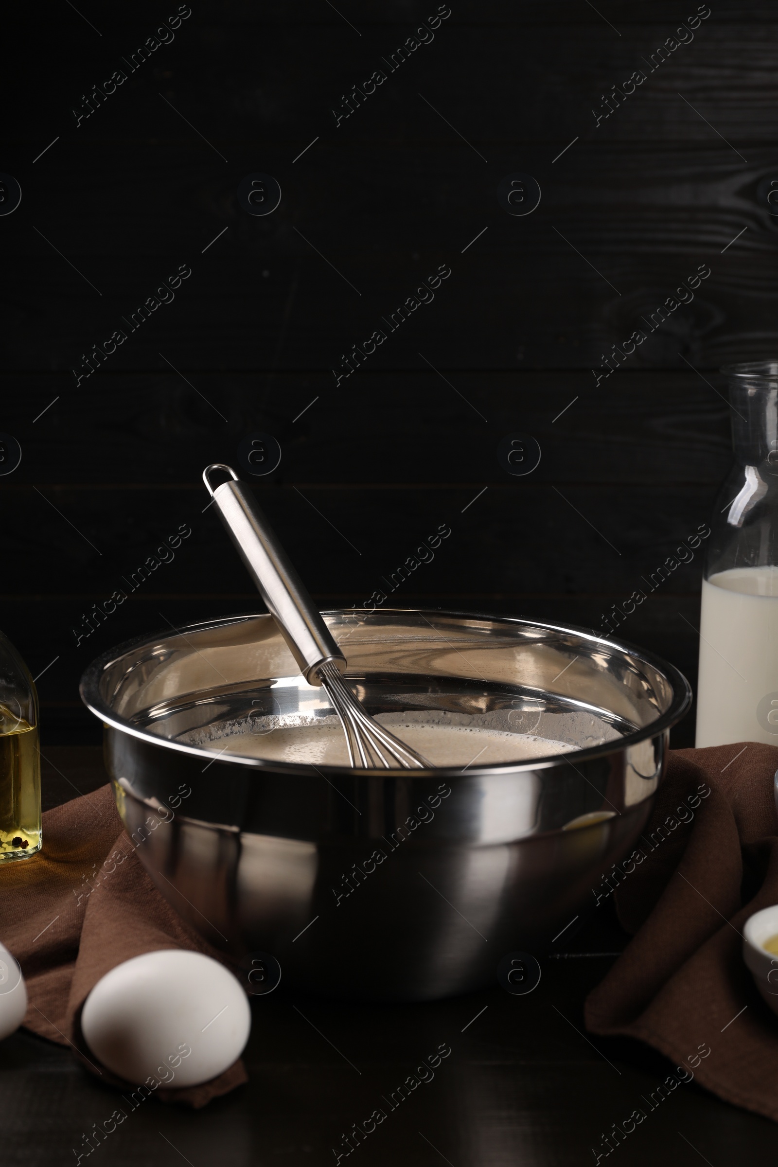 Photo of Composition with whisk and dough in bowl on table against dark wooden wall, space for text