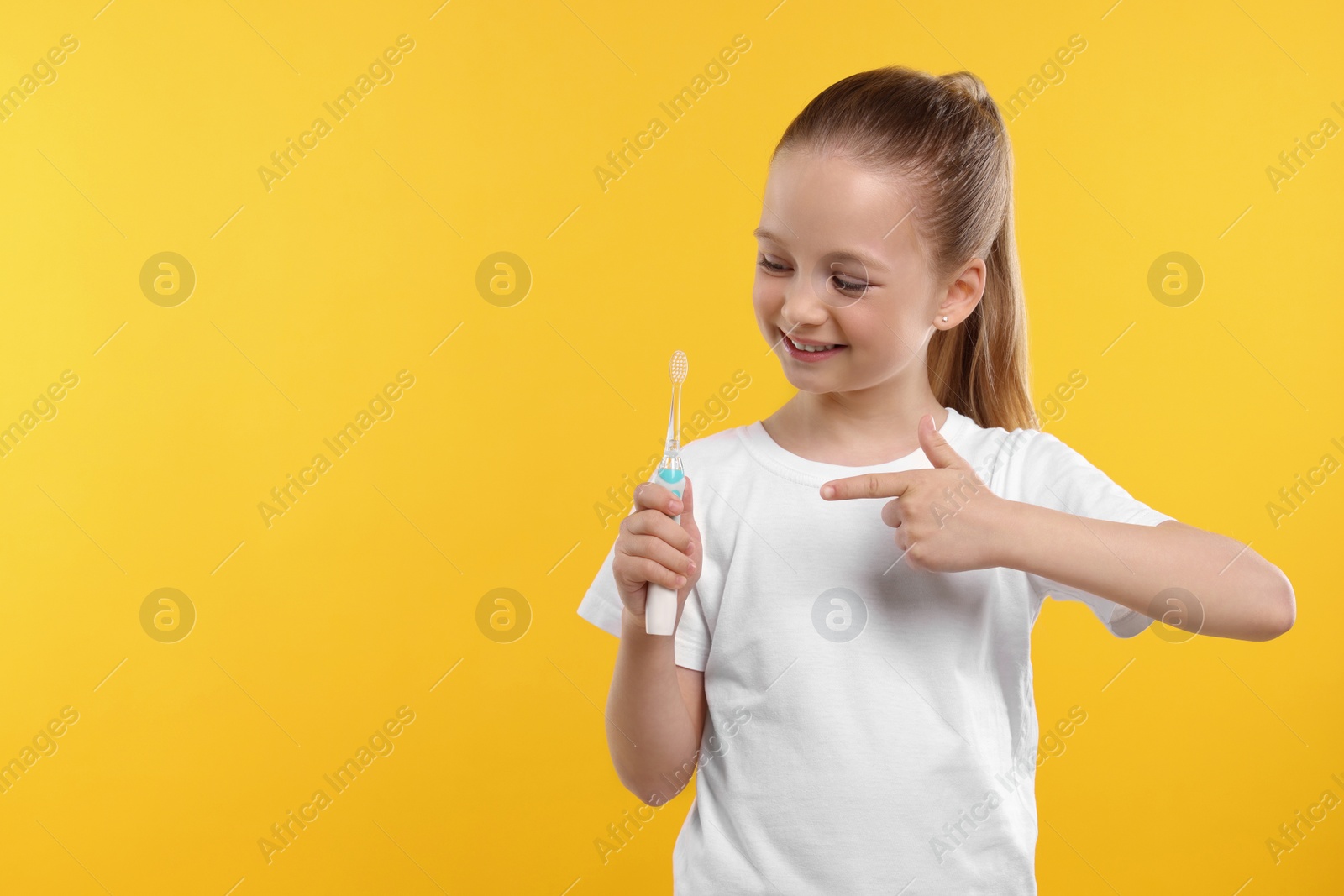 Photo of Happy girl holding electric toothbrush on yellow background. Space for text