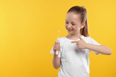 Happy girl holding electric toothbrush on yellow background. Space for text