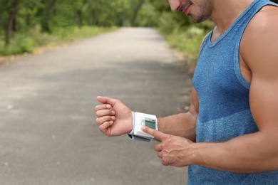 Photo of Young man checking pulse with medical device after training in park, closeup. Space for text