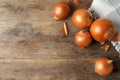 Photo of Ripe yellow onion bulbs on wooden table, flat lay. Space for text