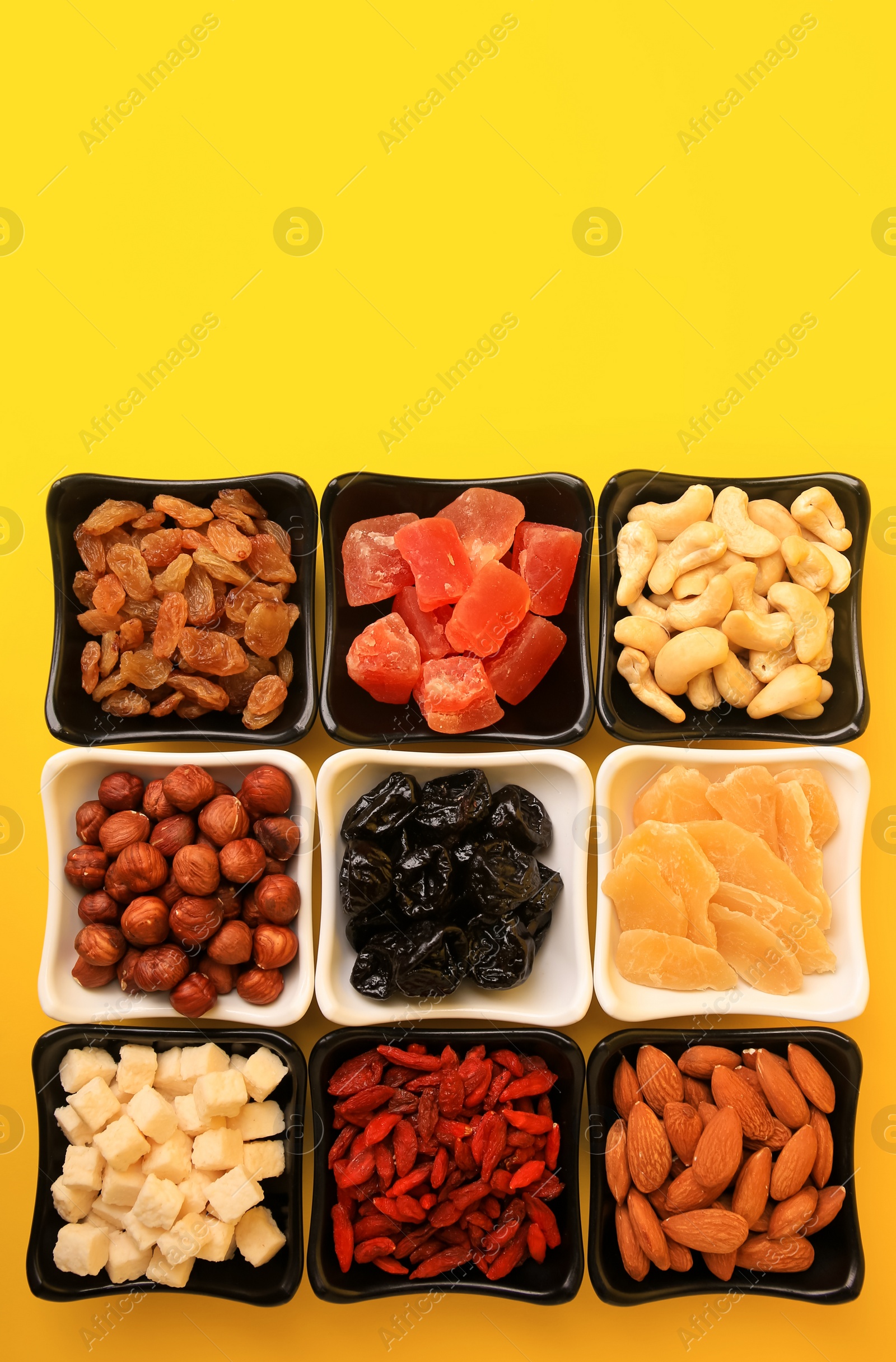 Photo of Bowls with dried fruits and nuts on yellow background, flat lay. Space for text