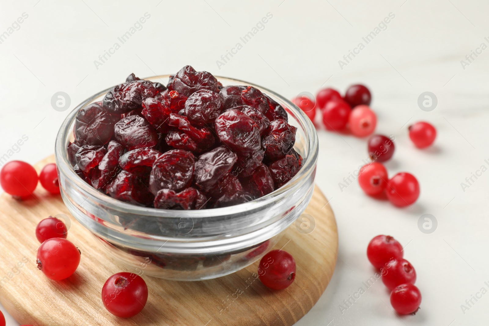Photo of Tasty dried cranberries in bowl and fresh ones on white table, closeup. Space for text