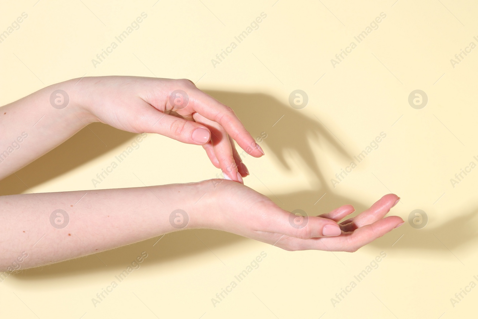 Photo of Woman applying cream on her hand against yellow background, closeup