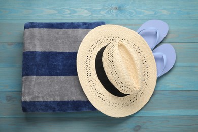 Beach towel, flip flops and straw hat on light blue wooden background, flat lay