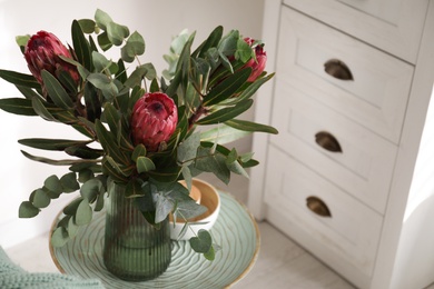 Photo of Vase with bouquet of beautiful Protea flowers on table in room
