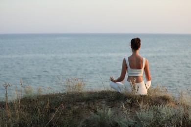 Woman meditating near sea, back view. Space for text