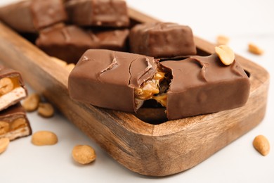 Wooden board of chocolate bars with caramel, nuts and nougat on white table, closeup