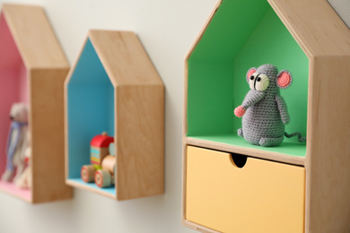 Photo of Knitted mouse on house shaped shelf indoors, closeup. Baby room interior design