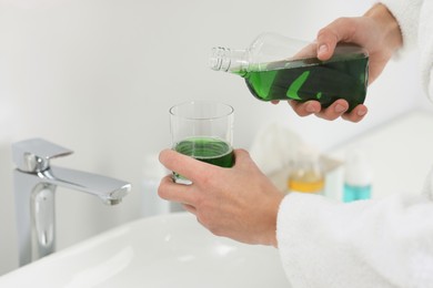 Photo of Young man using mouthwash in bathroom, closeup