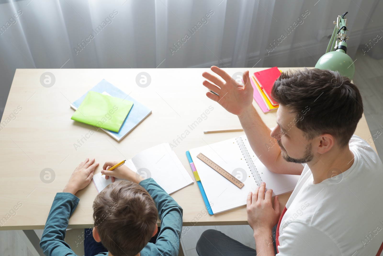 Photo of Dad helping his son with school assignment at home, above view