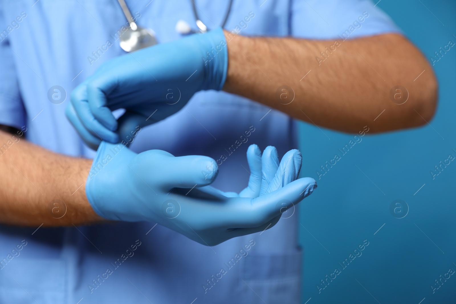 Photo of Doctor putting on medical gloves against blue background, closeup