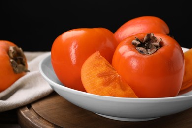 Photo of Delicious ripe persimmons on wooden board, closeup