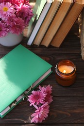 Book with beautiful chrysanthemum flowers as bookmark and candle on wooden table, above view