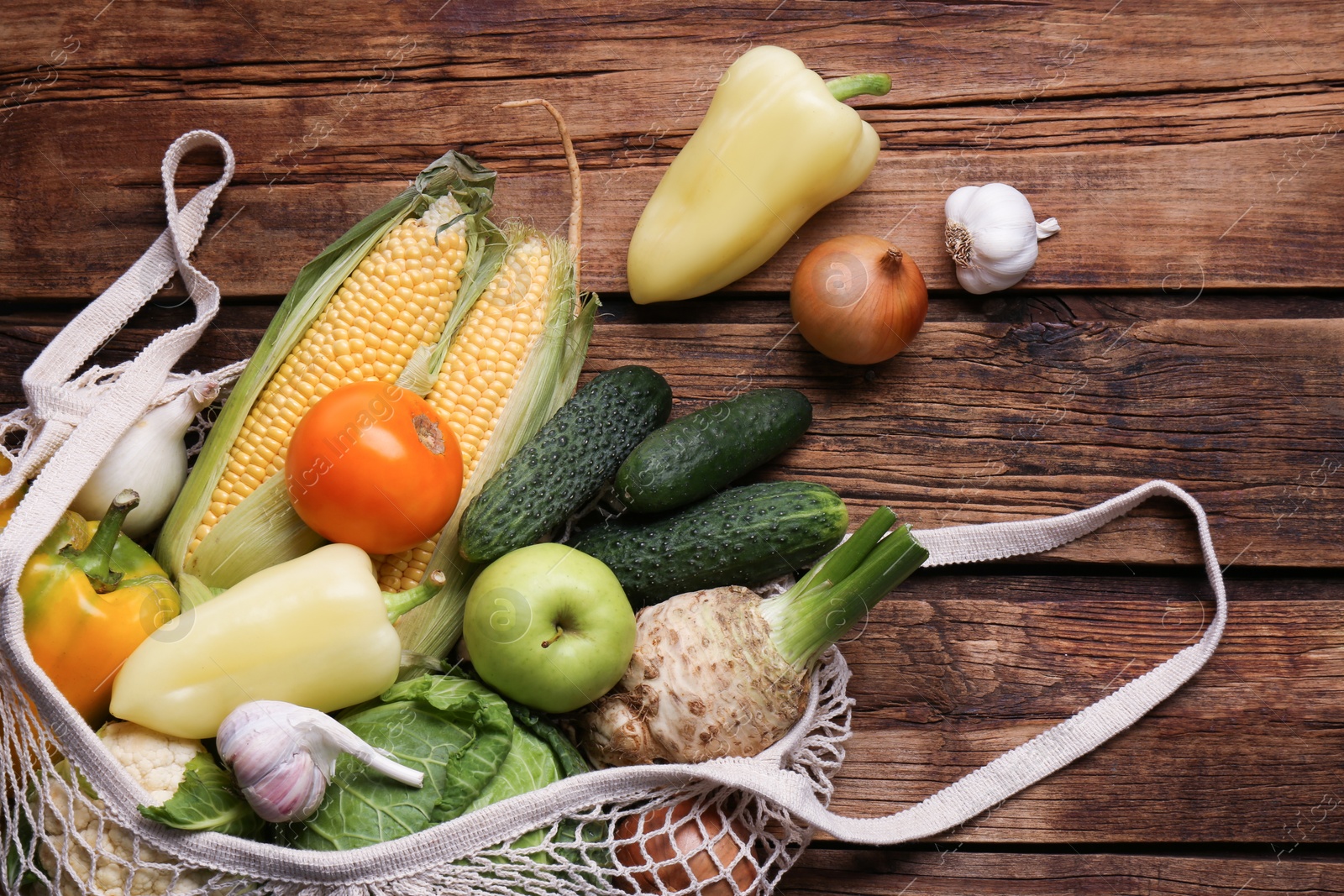 Photo of Different fresh vegetables in net bag on wooden table, flat lay. Farmer harvesting