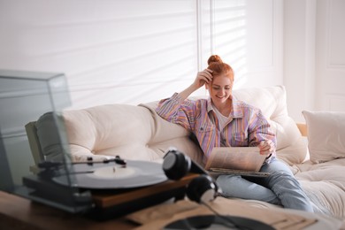 Young woman choosing vinyl disc to play music with turntable at home