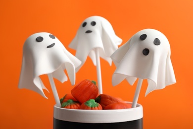 Photo of Delicious ghost shaped cake pops on orange background, closeup. Halloween celebration