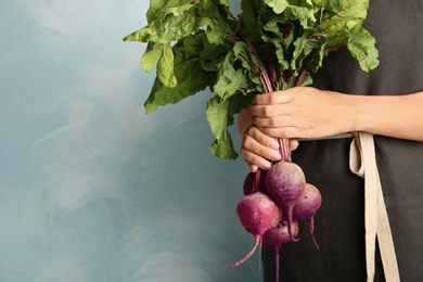 Young woman holding bunch of fresh beets on blue background, closeup. Space for text