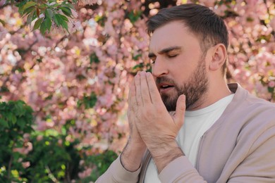 Photo of Man suffering from seasonal pollen allergy near blossoming tree outdoors