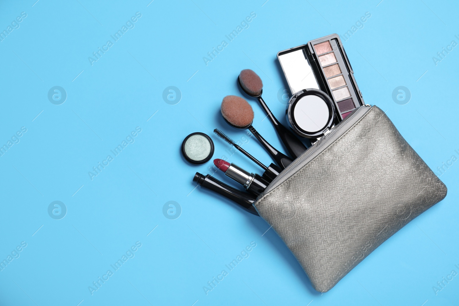 Photo of Cosmetic bag with makeup products and accessories on light blue background, flat lay. Space for text