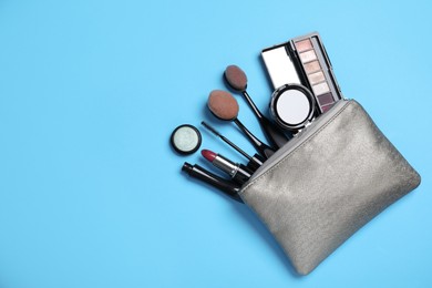 Cosmetic bag with makeup products and accessories on light blue background, flat lay. Space for text