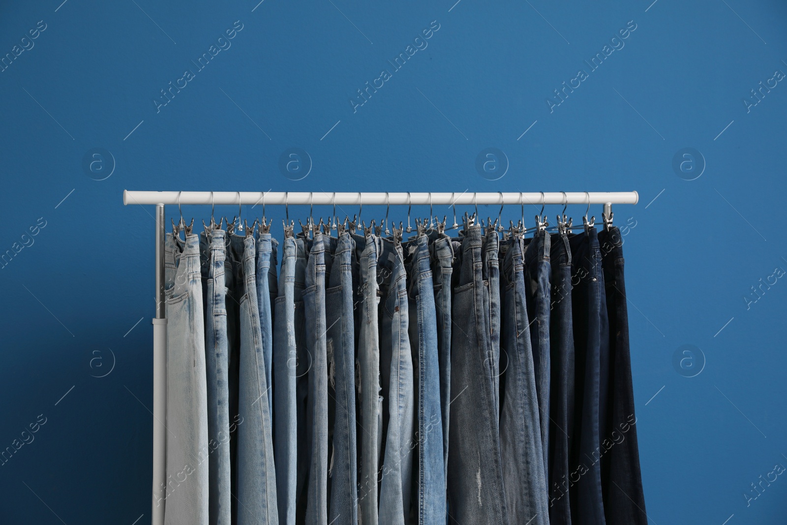 Photo of Rack with stylish jeans on blue background