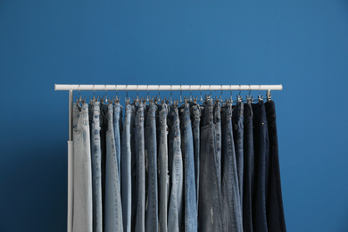 Photo of Rack with stylish jeans on blue background