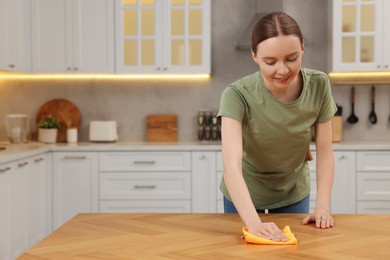 Woman with microfiber cloth cleaning wooden table in kitchen. Space for text
