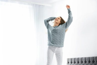 Photo of Young woman in warm sweater jumping on bed at home