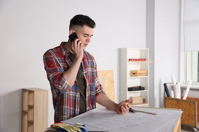 Photo of Handyman working with blueprints and talking on phone in room