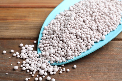 Chemical fertilizer in metal gardening shovel on wooden table, closeup