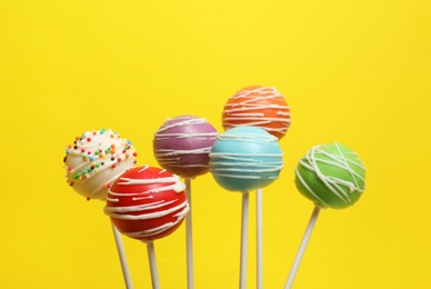 Many bright delicious cake pops on color background