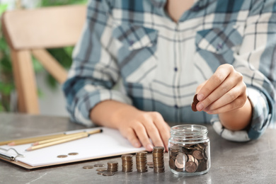 Photo of Woman putting money into glass jar at table, closeup