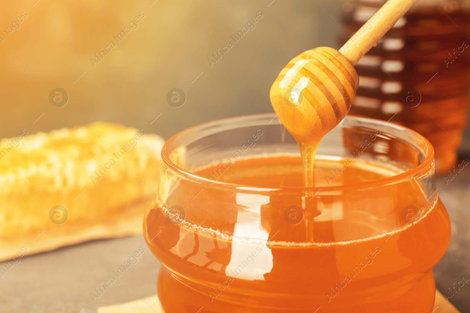 Image of Sweet honey dripping from dipper into glass jar, closeup