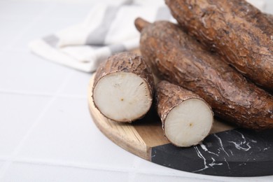 Whole and cut cassava roots on white tiled table, closeup. Space for text