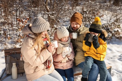 Family warming themselves with hot tea outdoors on snowy day