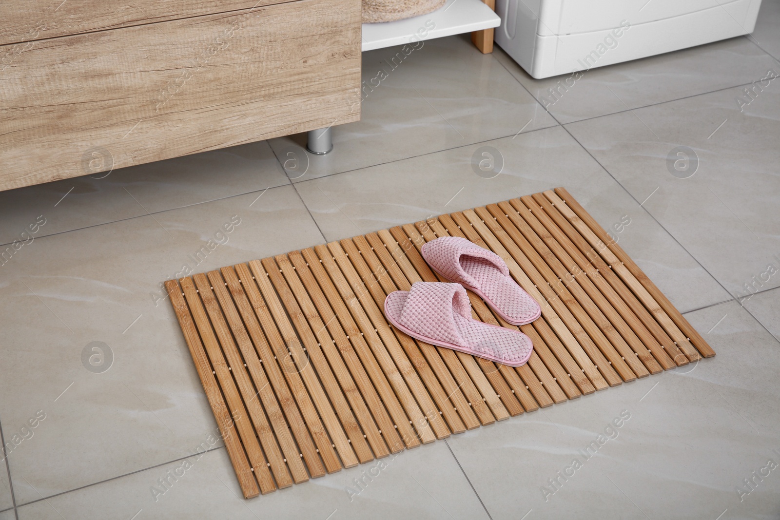 Photo of Wooden mat with slippers on floor in bathroom