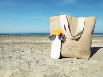 Photo of Bag, sunglasses and sun protection product on sandy beach. Space for text