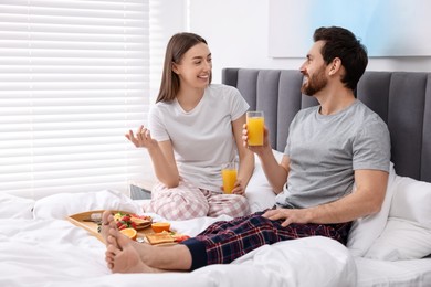 Photo of Happy couple having breakfast and talking on bed at home