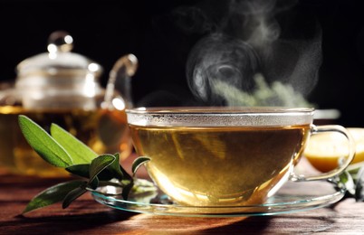 Cup of aromatic herbal tea and fresh sage on wooden table