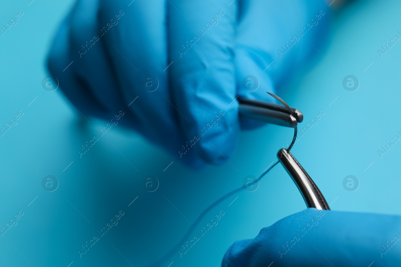 Photo of Professional surgeon holding forceps with suture thread on light blue background, closeup. Medical equipment