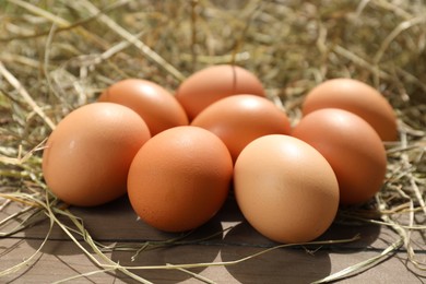 Fresh chicken eggs and dried hay on wooden table, closeup