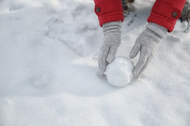 Photo of Young woman rolling snowball outdoors on winter day, closeup. Space for text