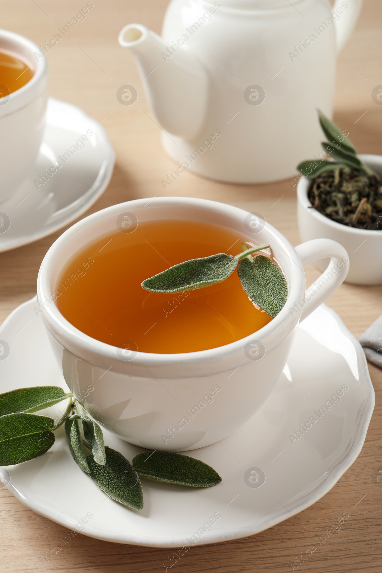 Photo of Cup of aromatic sage tea with fresh leaves on wooden table