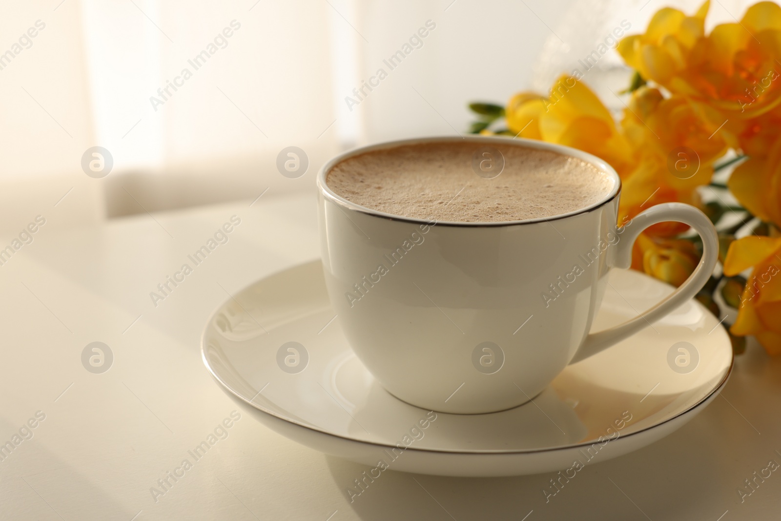 Photo of Delicious morning coffee and flowers on white table indoors, space for text