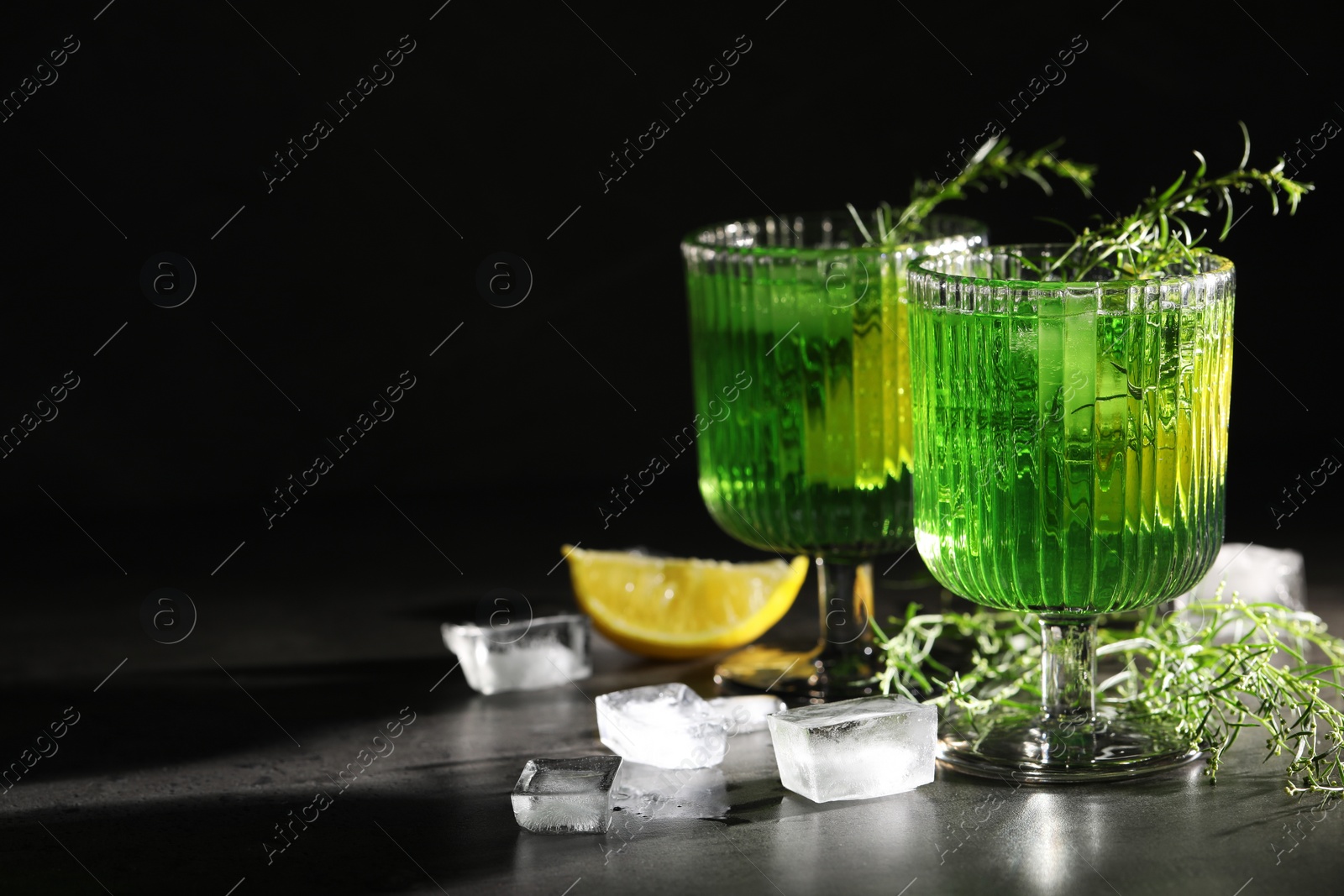 Photo of Glasses of homemade refreshing tarragon drink, ice cubes and sprigs on grey table, space for text