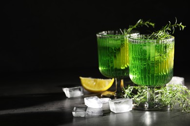 Photo of Glasses of homemade refreshing tarragon drink, ice cubes and sprigs on grey table, space for text