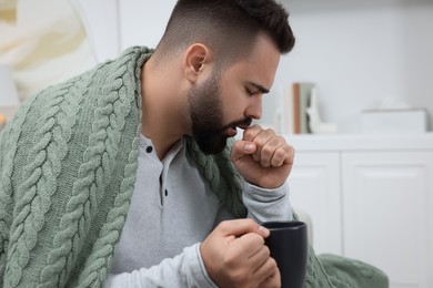 Sick man with cup coughing at home