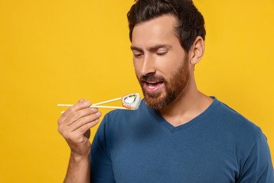 Photo of Handsome man eating sushi roll with chopsticks on orange background